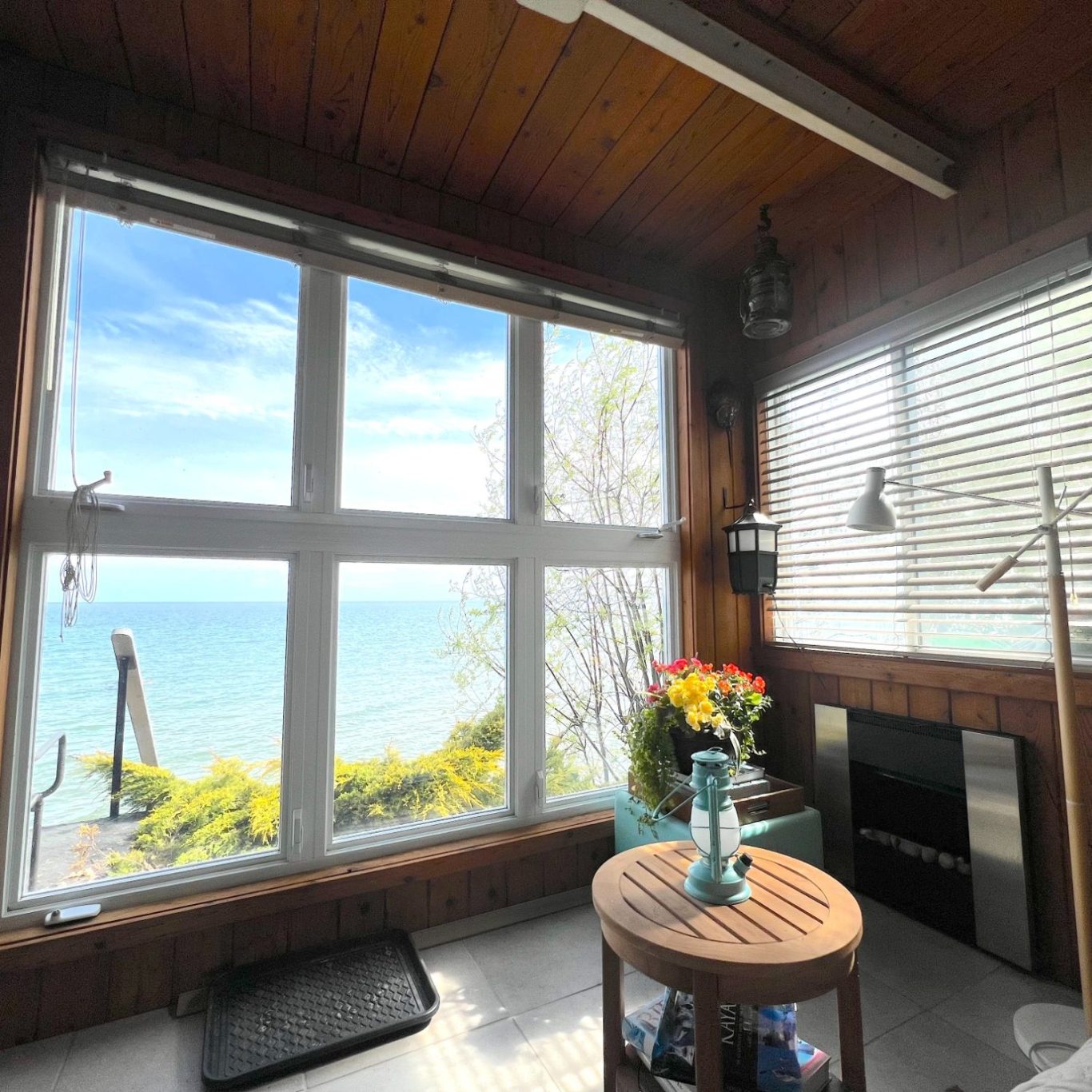 A cozy indoor hillside den featuring stained cedar wood paneling, an electric fireplace, and large panoramic windows looking out at Lake ON