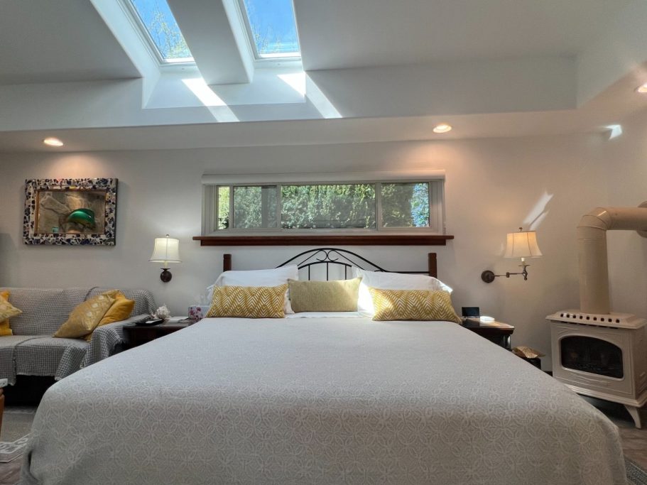 Stearns & Foster king bed centred under bright cathedral skylights with a bedside gas wood-stove in the luxury suite.