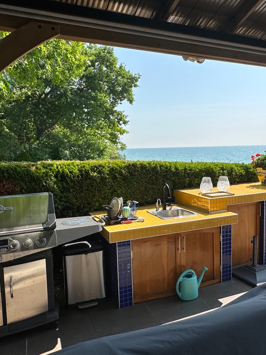 Outdoor kitchen with BBQ grill, yellow tiled countertop, and sink overlooking Lake Ontario at Wind in the Willows Oasis.