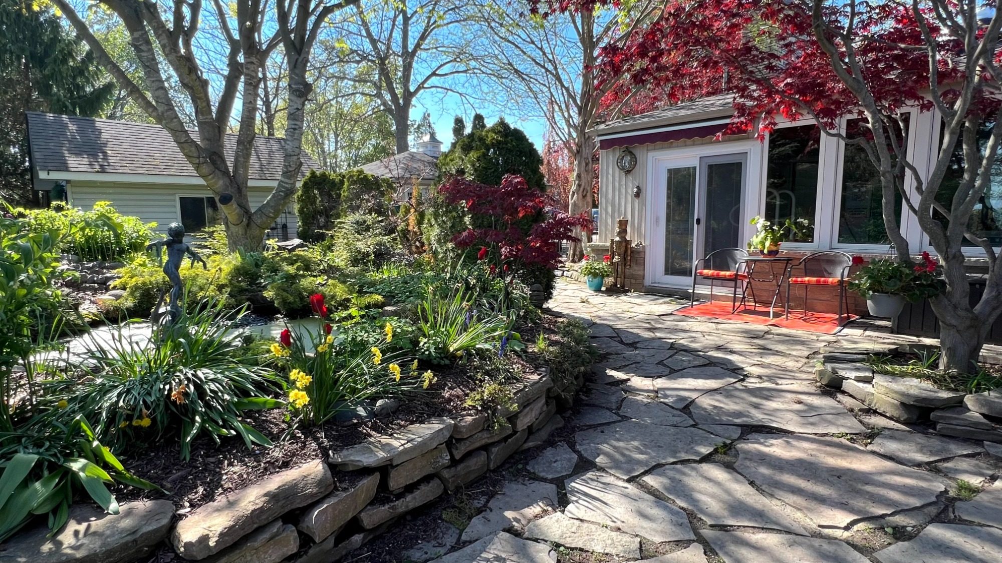 Flagstone patio walkway leading to the private guest suite entrance surrounded by lush spring gardens and mature trees at Wind in the Willow