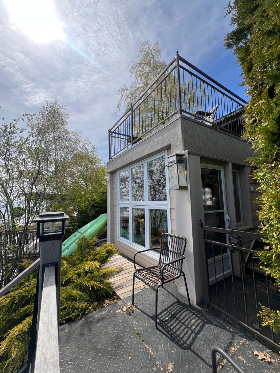 Exterior of the lakeside den built into the hillside, showing large panoramic windows and the upper patio deck above.